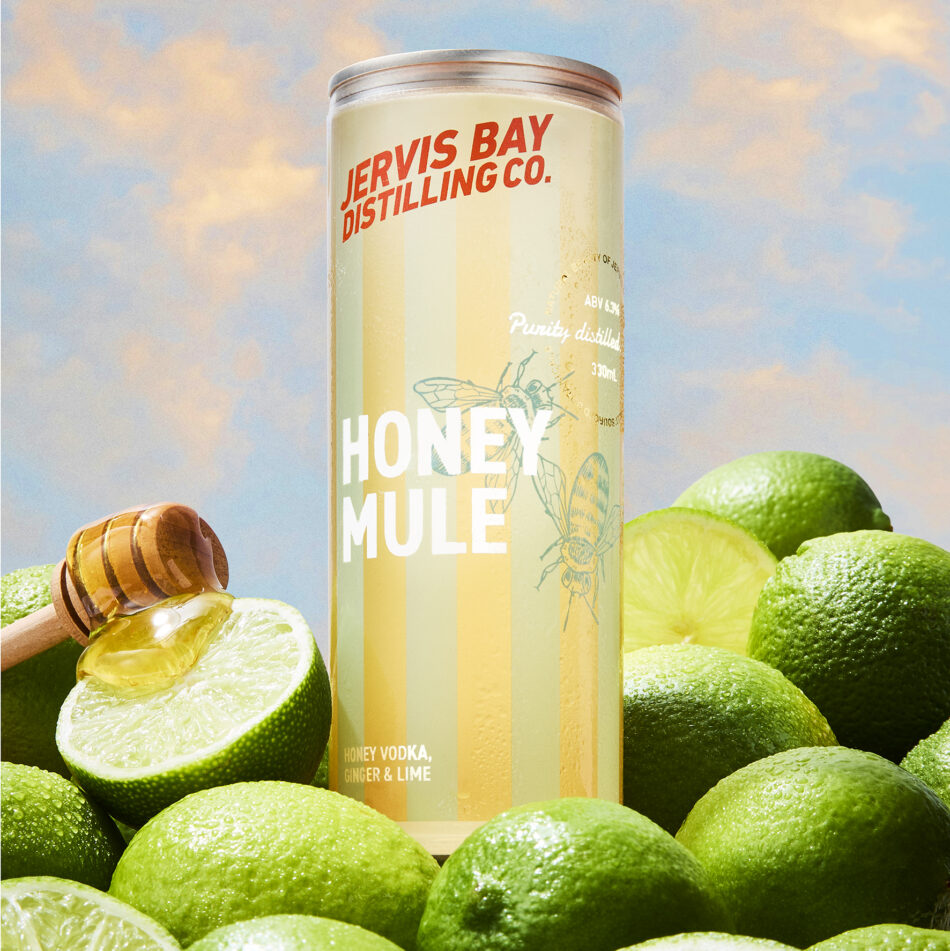 Jervis Bay Distilling Co. Honey Mule RTD can with limes and honey dipper at sunset sky